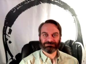 Close-up photo of Drew smiling sitting in a high-backed and padded black chair.