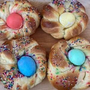 Photo of four round and braided challah bread loafs with brightly-colored hard-boiled eggs backed into the center of each.