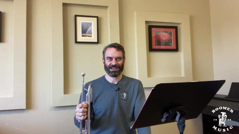 Photo of Drew holding his trumpet and smiling while seated behind a black music stand