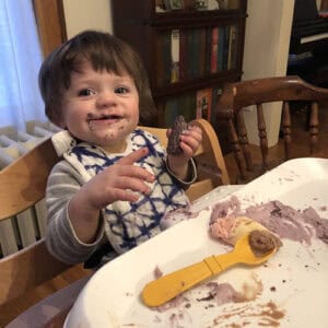 Photo of a young boy messily eating cake, smearing it on himself and a high chair.